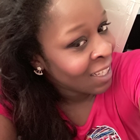 Aminah Washington, who is wearing a red shirt and has long hair, smiles at the camera.