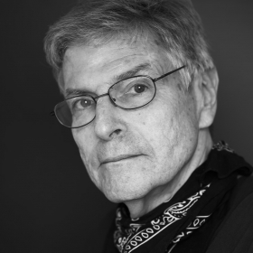 John Calendo, a man with a button down shirt and oval glasses, looks seriously at the camera. The photo looks modern but is in black and white.