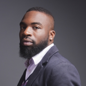 Darnell Moore, a man with a beard wearing a suit looking at the camera with a serious expression.