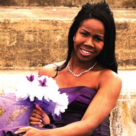 Eyricka Morgan, a young Black woman with long black hair. She is wearing a necklace, a purple sleeveless dress, and holding a bouquet of flowers.