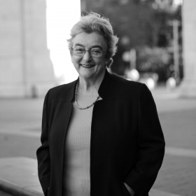 Miriam Frank, an older woman with short hair and glasses, poses outdoors. The photo looks modern but is black and white.