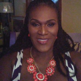 Angie Raine, a woman wearing a black and white dress and an orange necklace, smiling into the camera