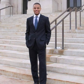 Czezre Adams, a young man wearing a suit and blue tie, stands on the steps in front of a building.