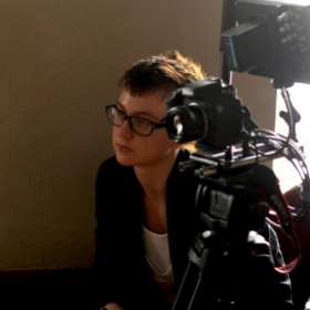 Blair Walter, who has short brown hair and glasses, is crouched next to video recording equipment.