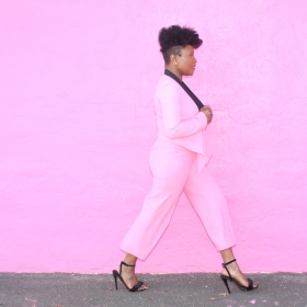 Lynette Lashawn, a Black woman wearing a pink suit, stands in front of a pink wall.