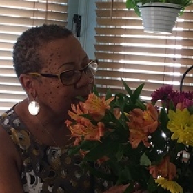 Saundra Toby Heath, who has short hair and glasses, smelling a bouquet of flowers.