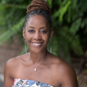 Tamara Fleming, who has her hair in a bun, smiles at the camera. She is wearing a blue and white dress and a necklace.