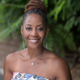 Tamara Fleming, who has her hair in a bun, smiles at the camera. She is wearing a blue and white dress and a necklace. 